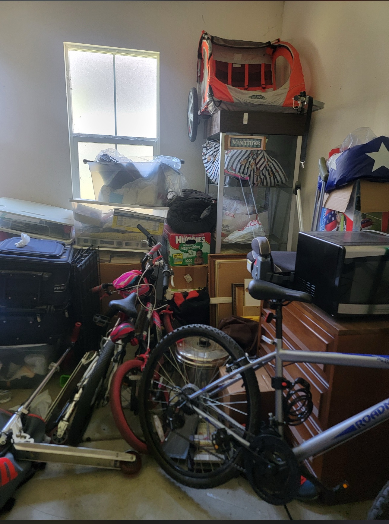 Before: cluttered Anaheim garage corner with bikes, bins, boxes and a microwave