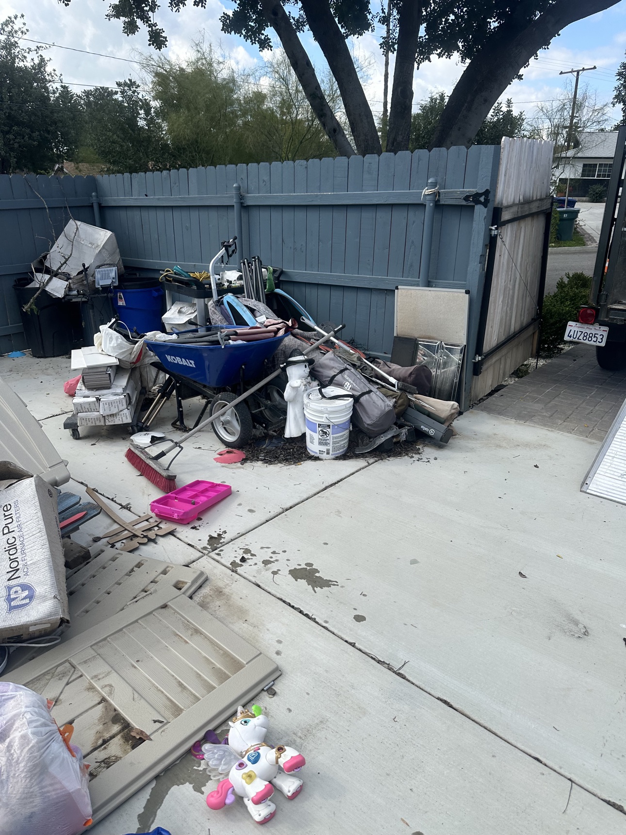 Before: cluttered Moreno Valley patio corner with a wheelbarrow, stacked tiles, tools and storage bins